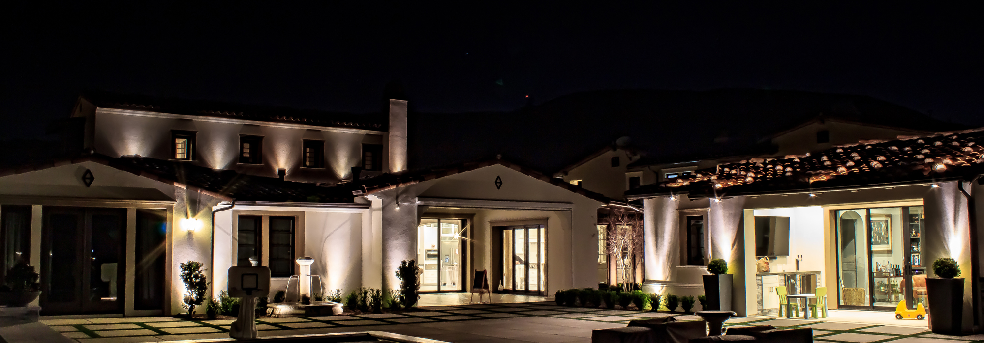 Elegantly lit home exterior with architectural uplighting and landscape lighting that boosts curb appeal at night